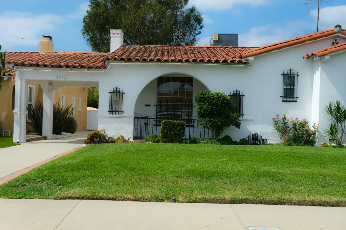 A white single-story house with a red tile roof and a green front lawn