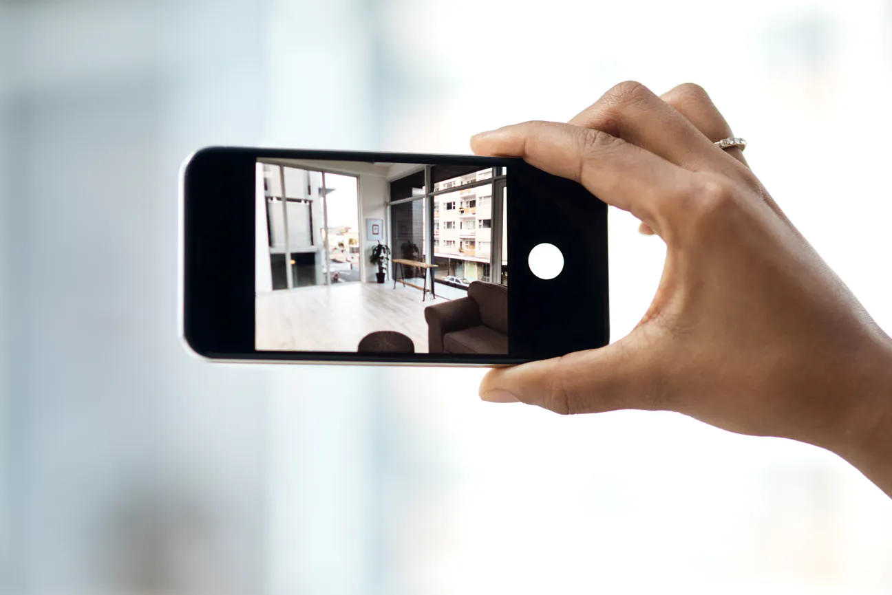 A hand holding a phone, photographing a room.