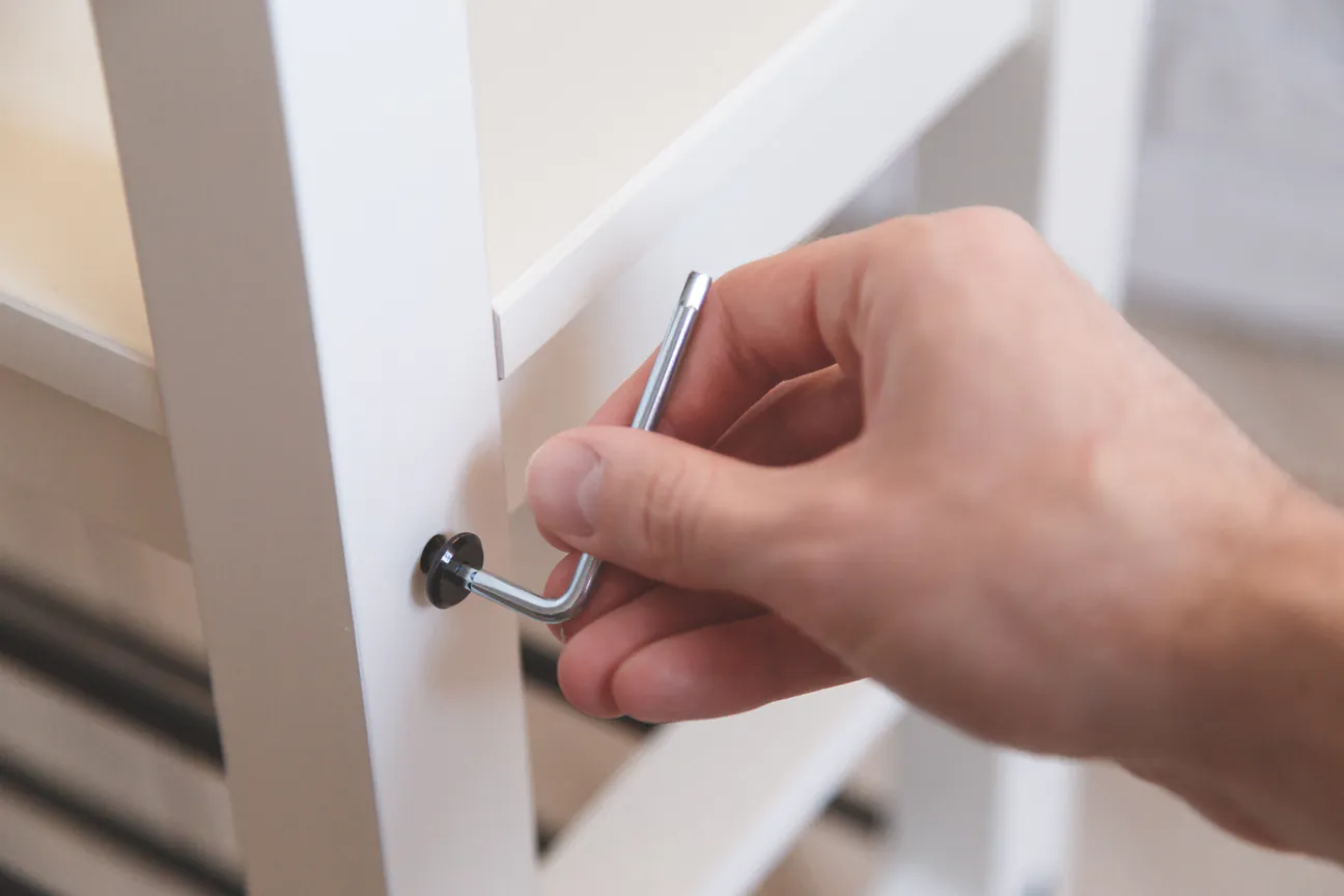 A hand turning an allen key into a white furniture frame