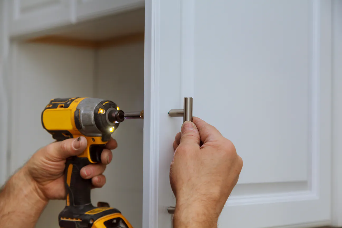 An impact driver fastening a new bar pull to a white cabinet door