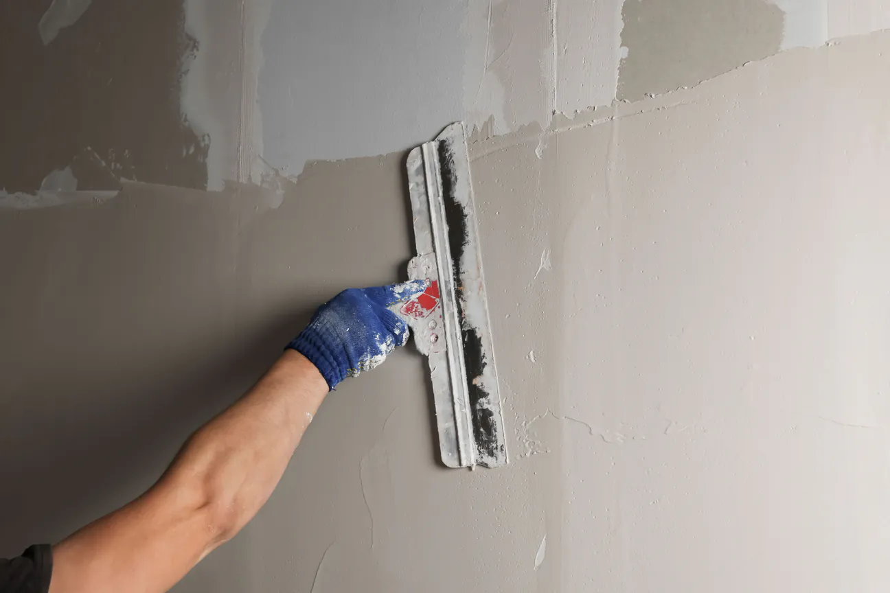 A wide taping knife spreading joint compound across a wall