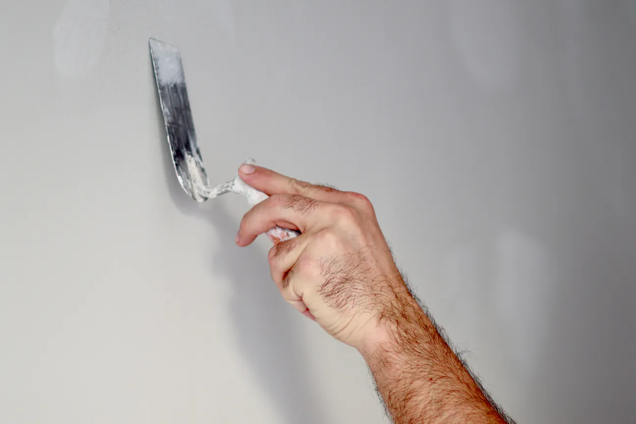 A hand working putty onto a wall with a trowel