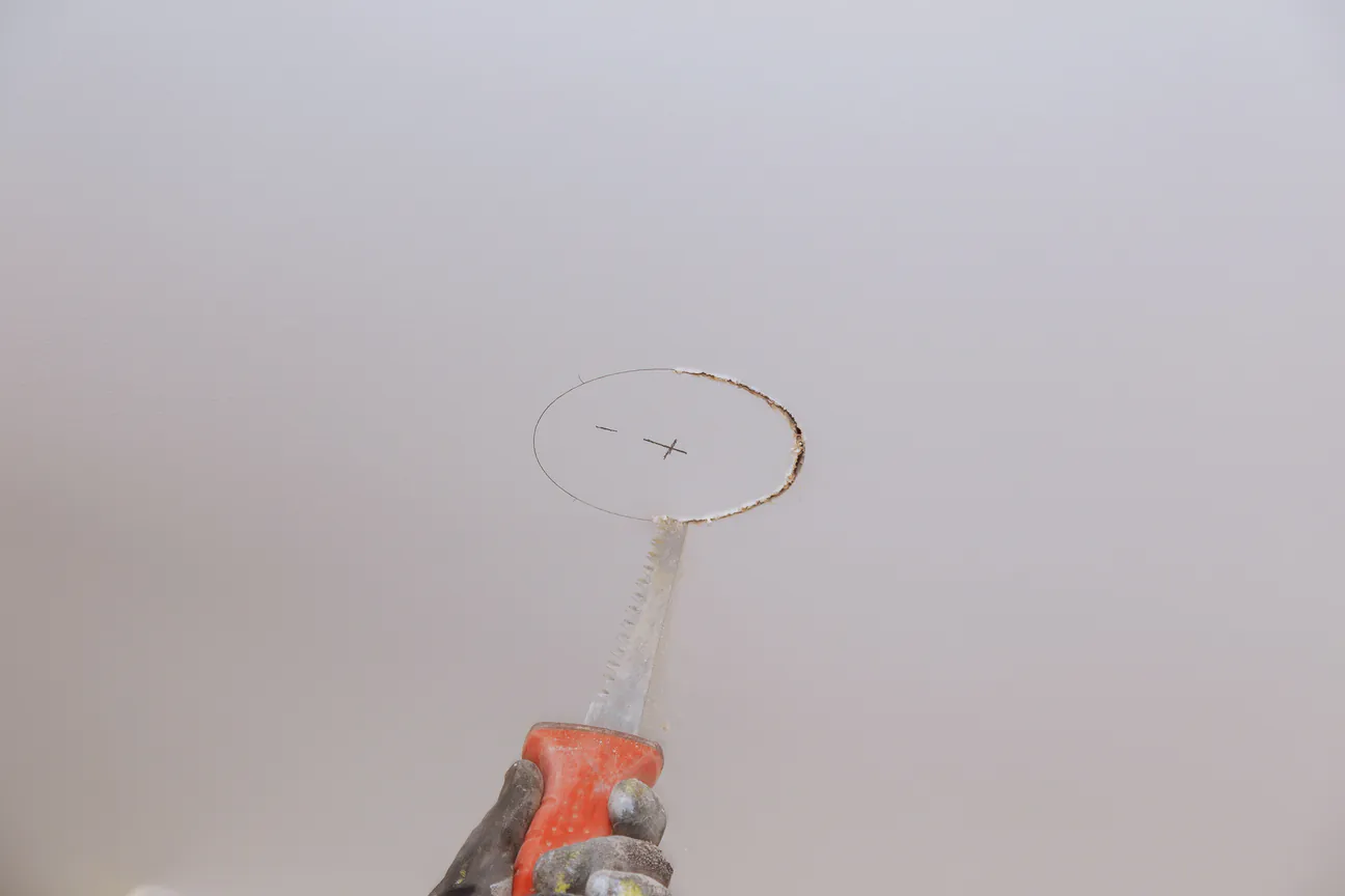 Drywall saw cutting out a marked section of a ceiling
