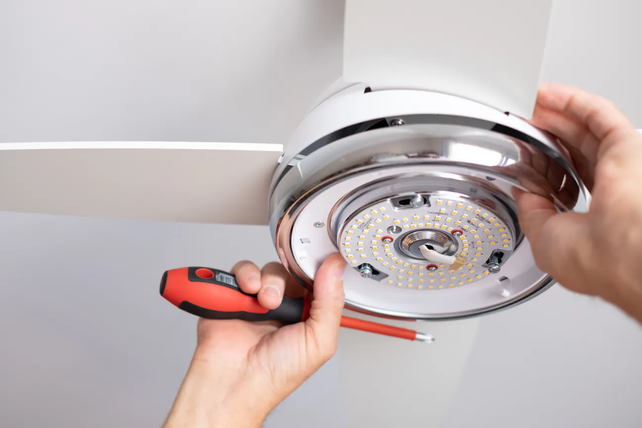A screwdriver fastening the underside of a new white ceiling fan