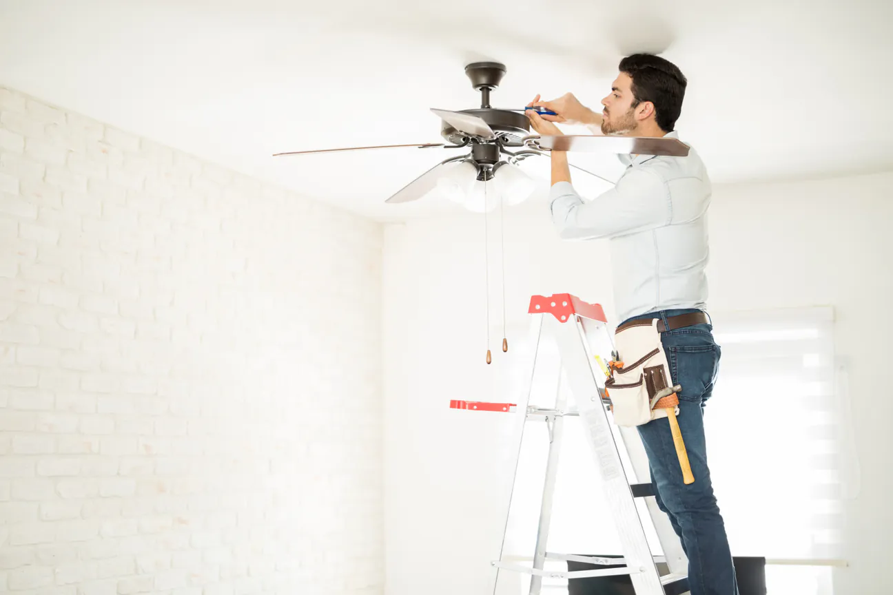 A worker on a step ladder fitting a ceiling fan