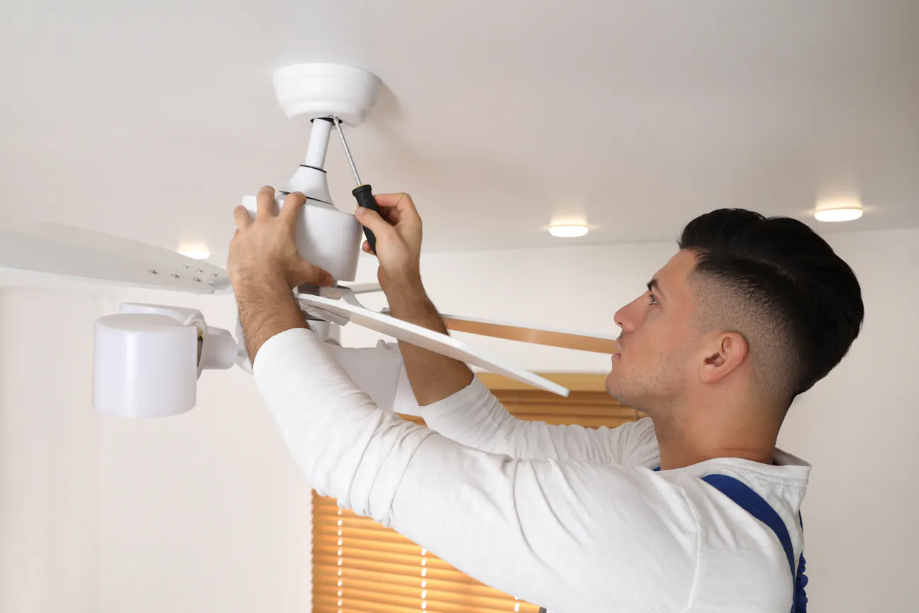 A new white ceiling fan being fixed to its mount with a screwdriver