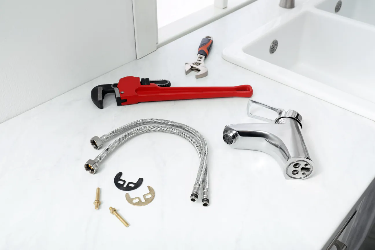 A new chrome faucet, braided supply lines and mounting hardware laid out beside a sink