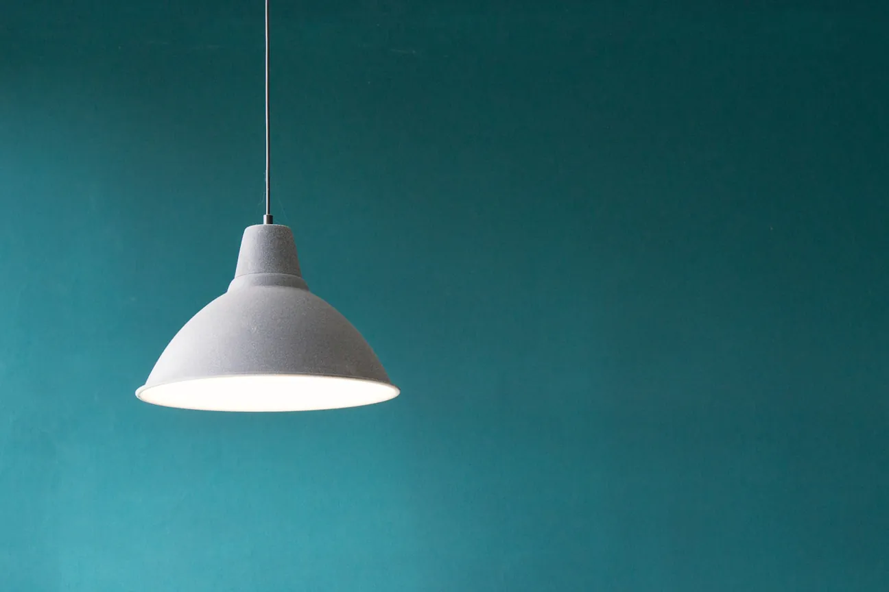 A pendant light hanging on a cord in front of a teal wall