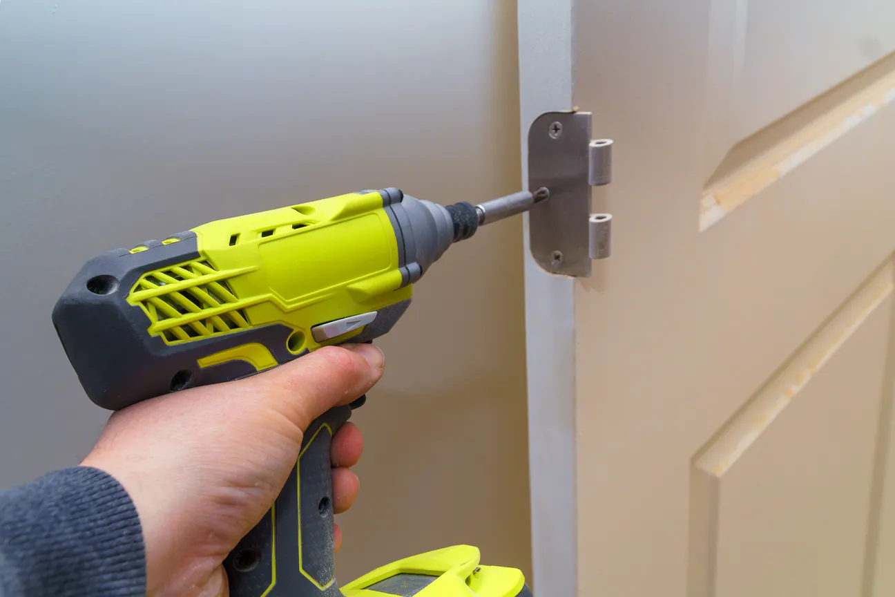 A cordless driver setting a hinge onto a door frame