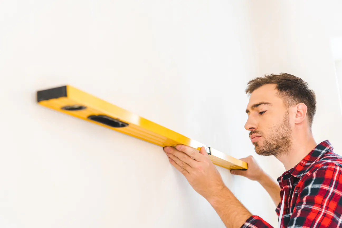 A man holding a spirit level flat against an interior wall