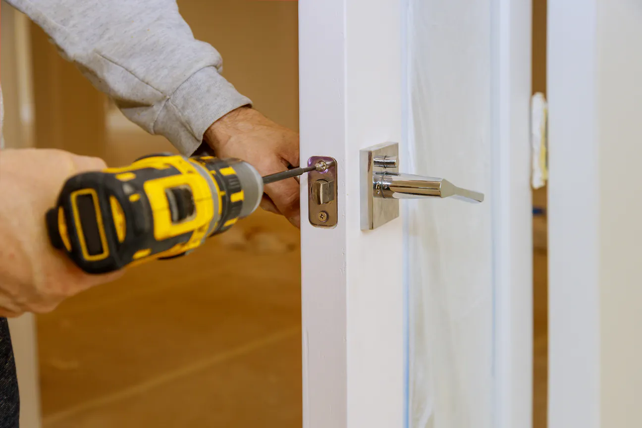 A cordless driver setting the latch plate into the edge of a white door