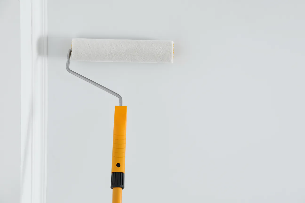 A roller on a long pole spreading white paint across a ceiling