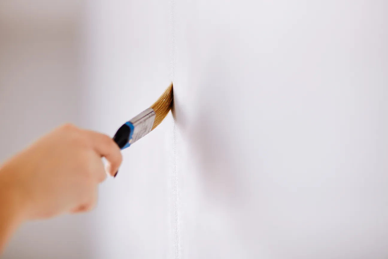 A hand cutting in along a wall edge with a paint brush