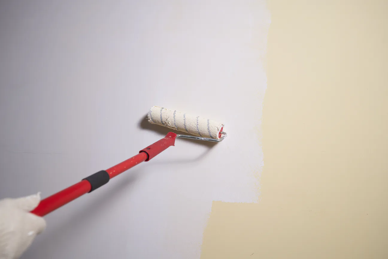 A paint roller rolling a fresh coat over an older wall color