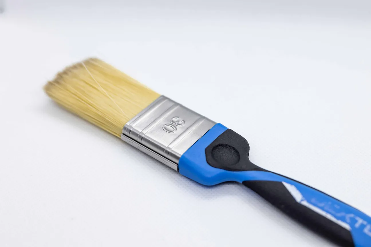 A trim brush with a blue handle resting on a white surface