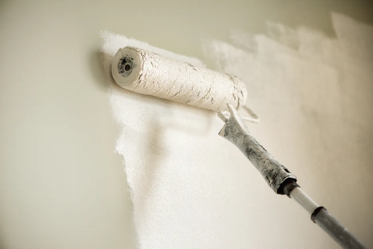 A roller putting a blue gray coat of paint across a white wall
