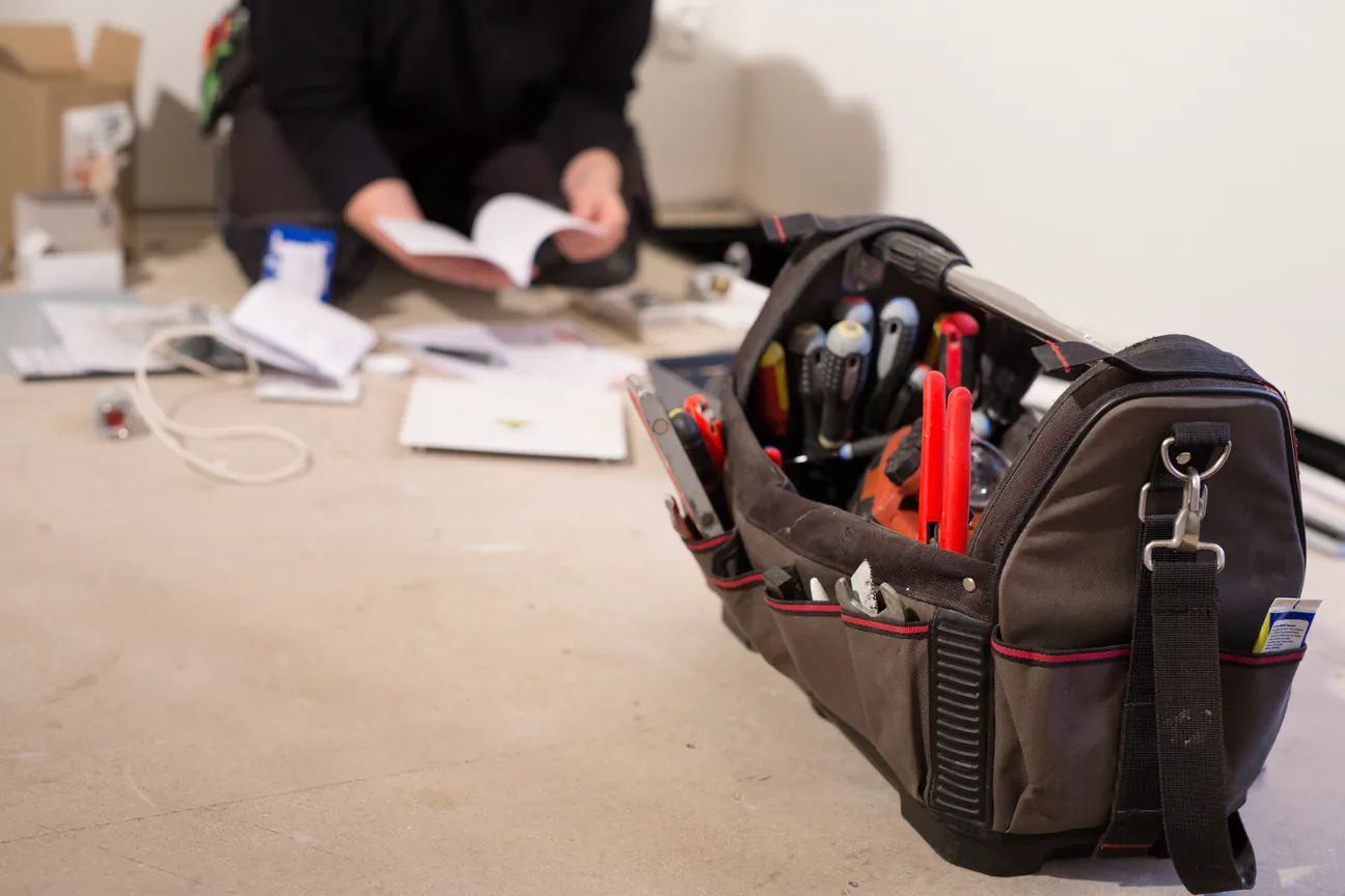An open tool bag on the floor with tools upright inside it