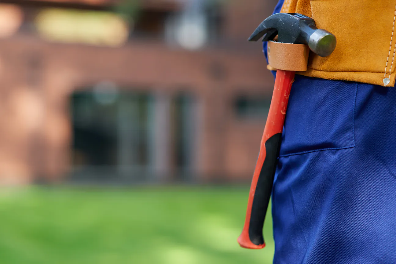 A hammer hanging in a leather tool belt outside a house