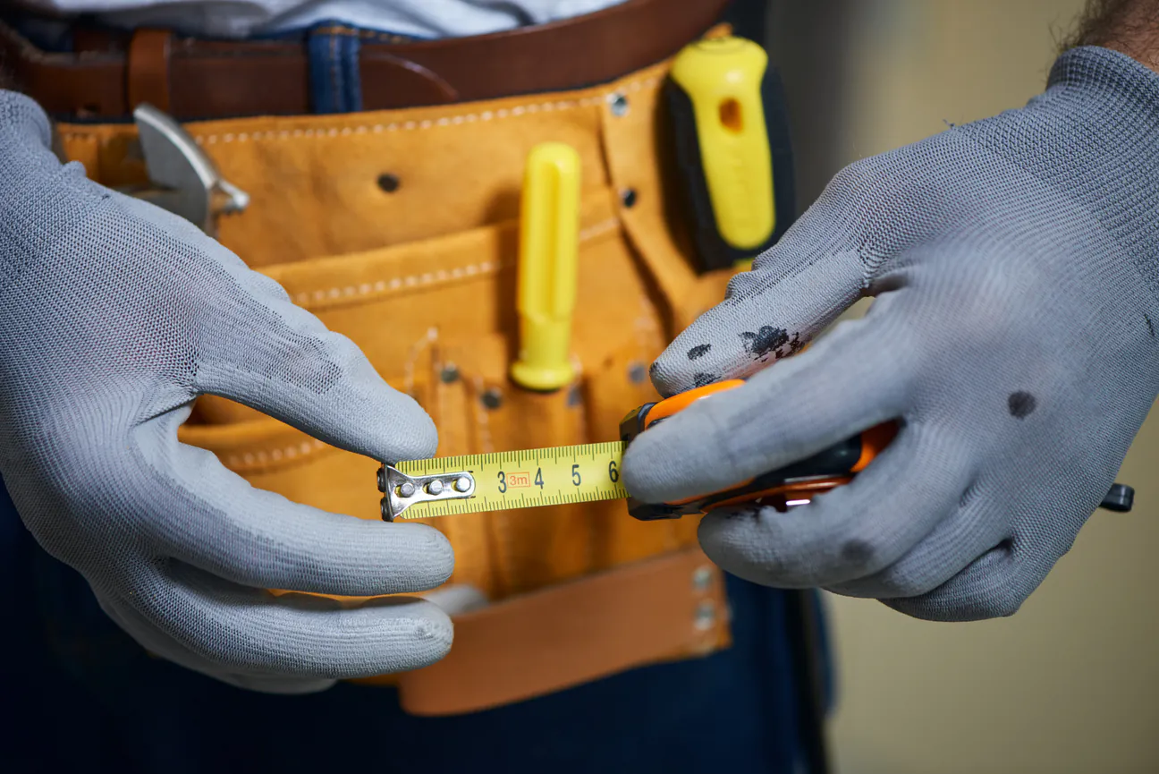 Gloved hands pulling out a tape measure in front of a loaded tool belt